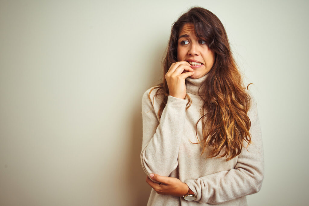 young beautiful woman wearing winter sweater standing over white isolated background looking stressed and nervous with hands on mouth biting nails. anxiety problem.
